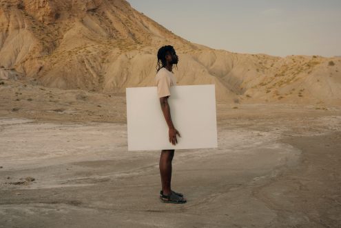 Person holding blank canvas in desert for mockup, side view, space for design, natural light, creative asset.